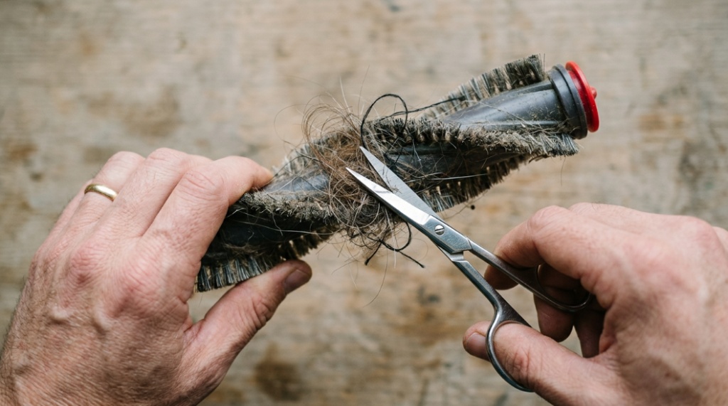 Close-up of hands using scissors to cut tangled hair off a vacuum cleaner roller brush.