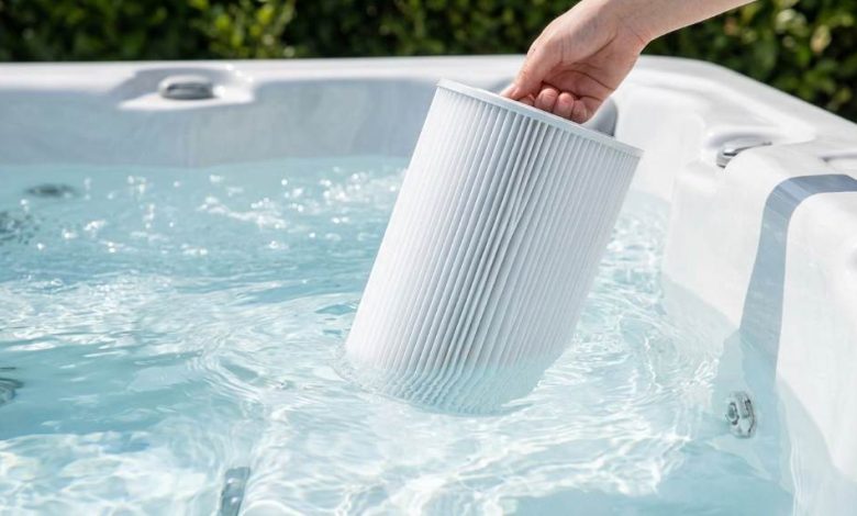 Person rinsing a hot tub filter cartridge with a garden hose outdoors