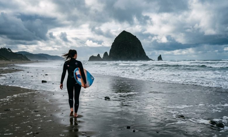 A skimboarder glides across wet sand with Oregon coastal sea stacks in the background.