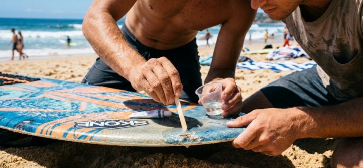 Person applying epoxy resin to fix a skimboard rail ding.