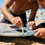 Person applying epoxy resin to fix a skimboard rail ding.