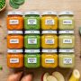Overhead view of organized glass jars filled with colorful homemade baby food purees.